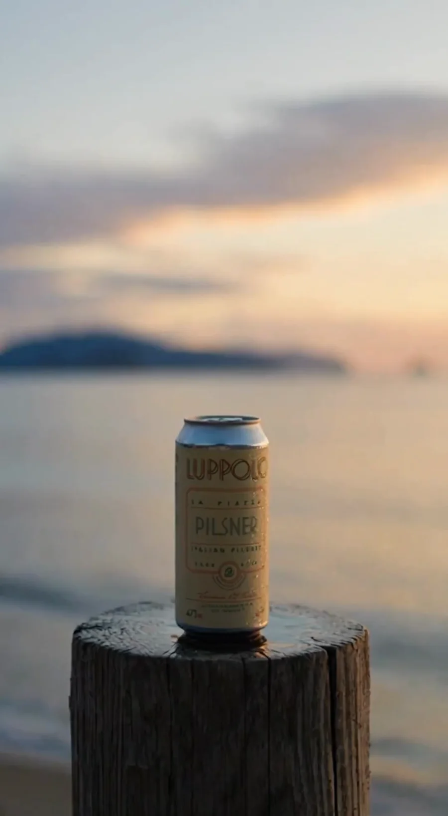 A Luppolo La Piazza Pilsner can resting on a weathered post at dusk — a frame from the campaign